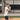 Baseball player at bat wearing a tan short-sleeve hoodie and black shorts, equipped with white batting gloves and a wood bat, ready for practice on a sunny day.